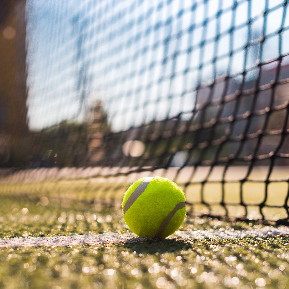 Closeup tennis ball lying on white line on hard court next the netting