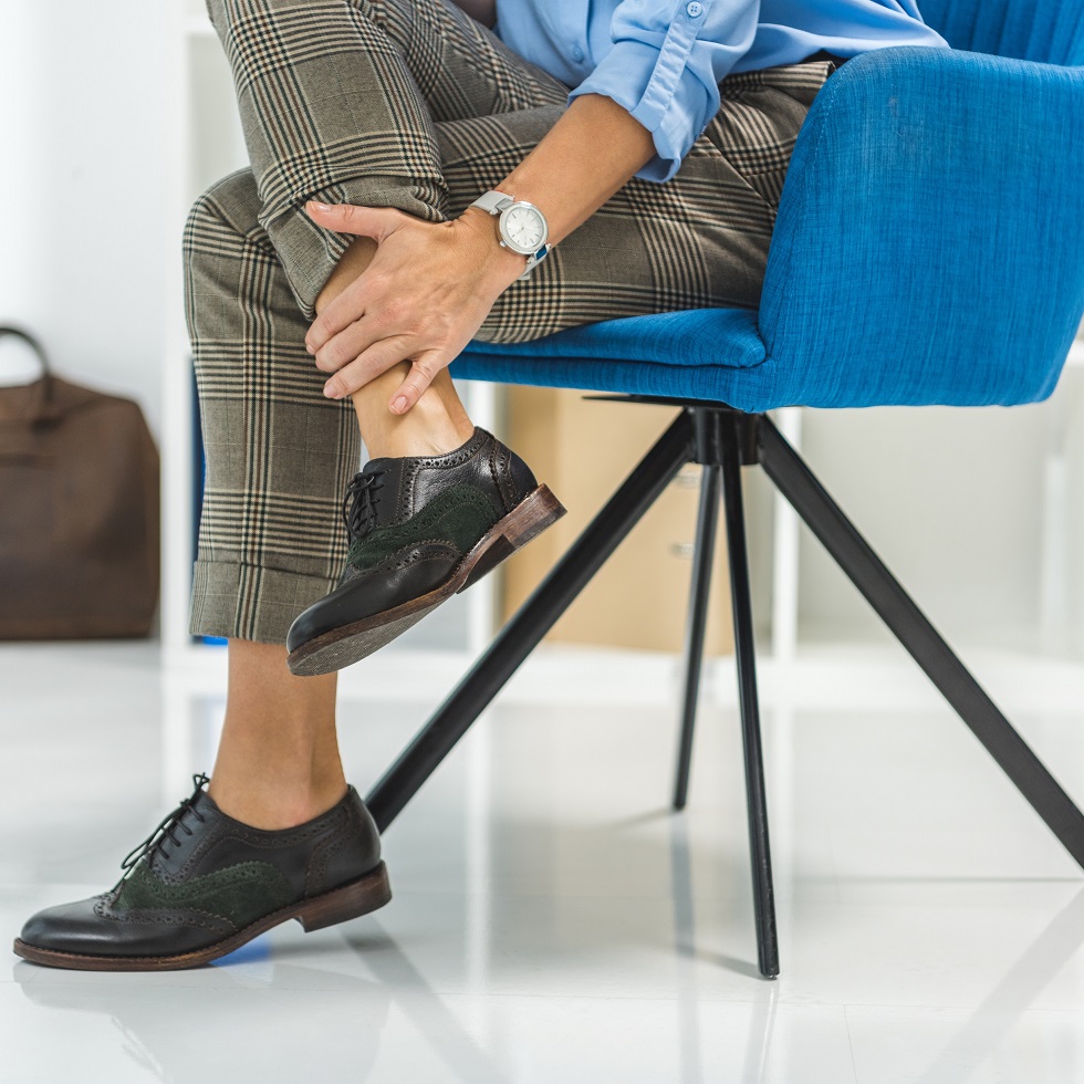 cropped view of tired businesswoman with painful legs sitting in chair